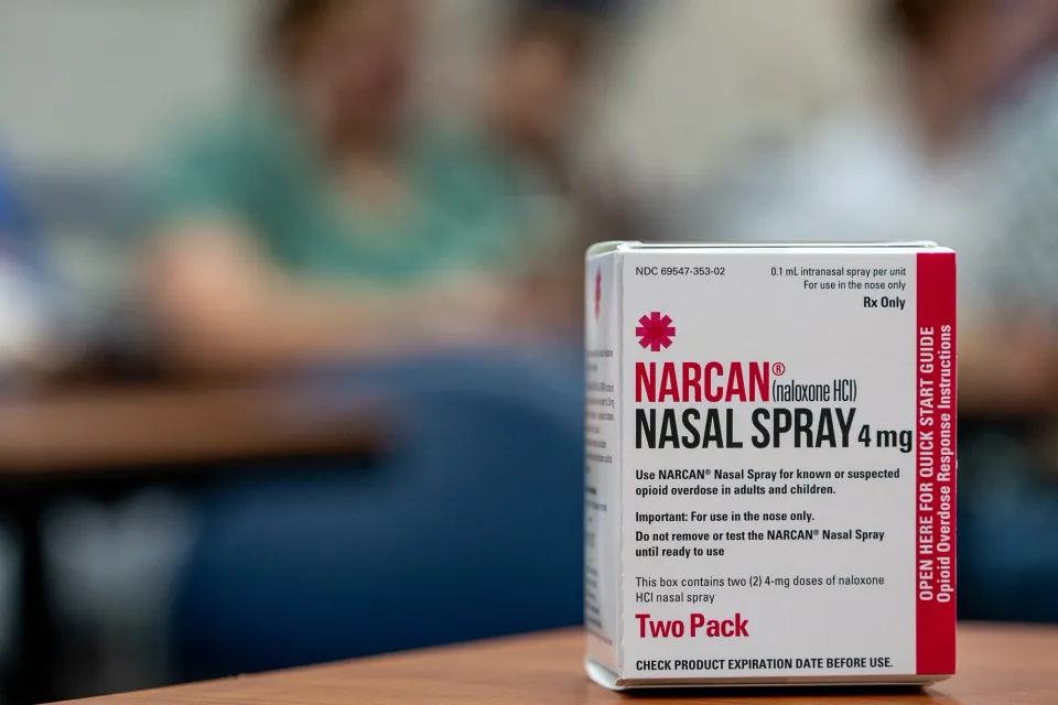 A box of narcan nasal spay sitting on a table against a blurred background of a classroom.